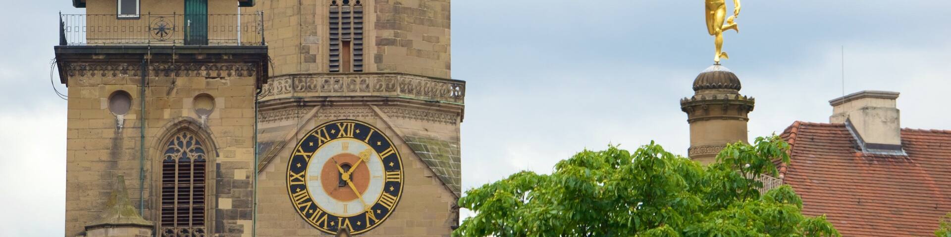 A historic tower with a clock, a bell tower, and a golden statue.