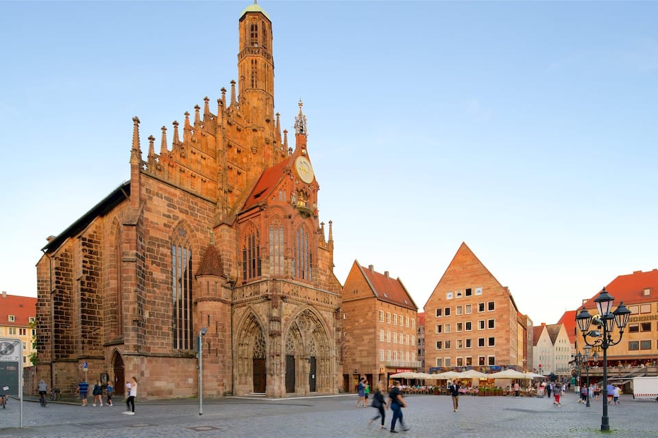 Een historische kathedraal met gedetailleerde gotische architectuur, een opvallende klokkentoren en een levendig plein met voetgangers en cafés.