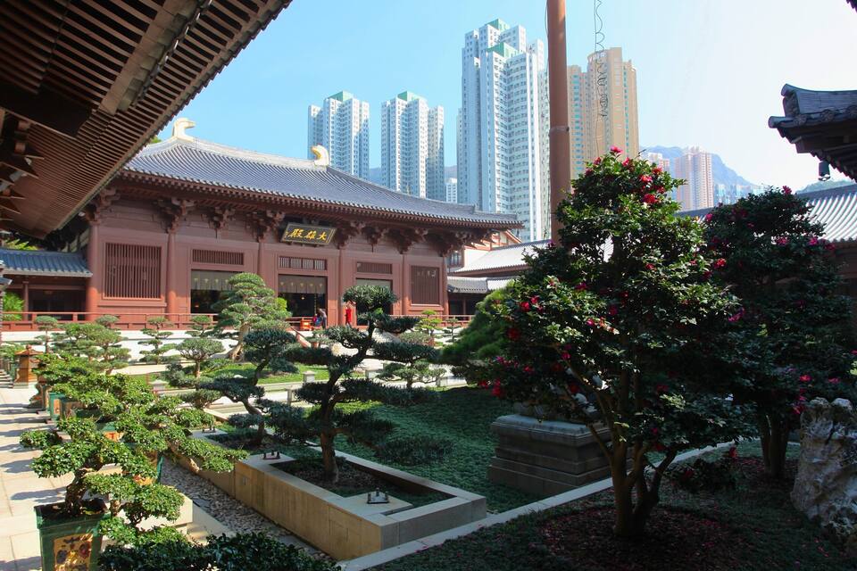 A traditional building with a tiled roof, surrounded by a well-maintained garden with various trees and a stone pathway.