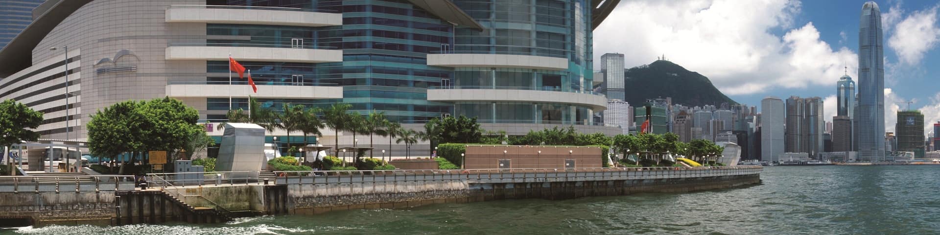 A modern architectural building with a curved design, situated by a waterfront with a cityscape in the background.