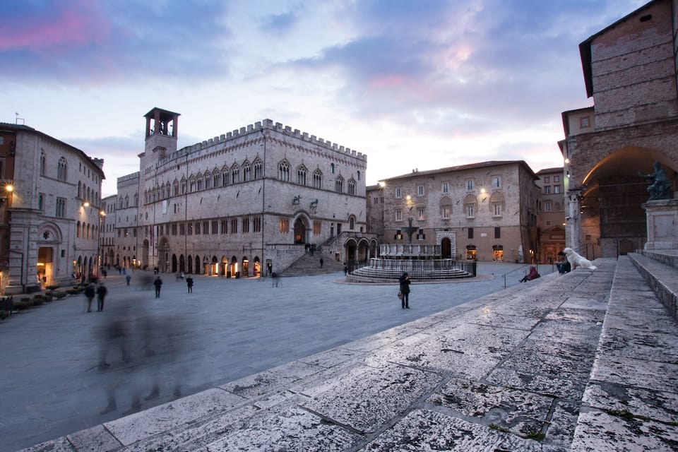 A historic square with a prominent building featuring a clock tower, surrounded by other classical architecture.