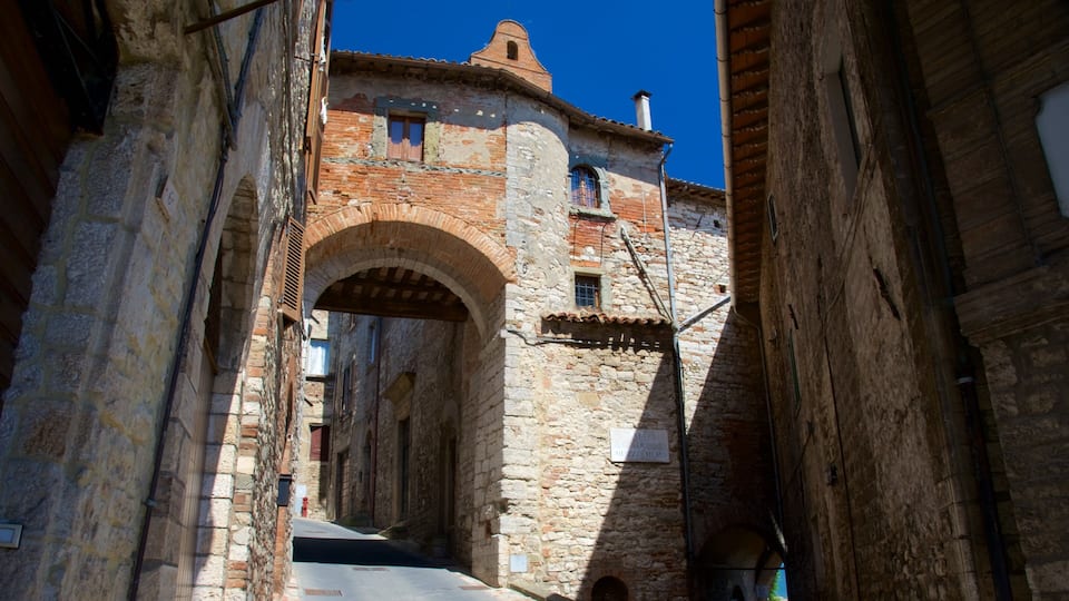 A narrow street with stone buildings, an arched gateway, and a clear blue sky.
