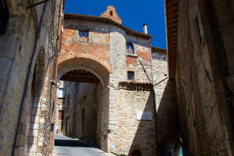 A narrow street with stone buildings, an arched gateway, and a clear blue sky.