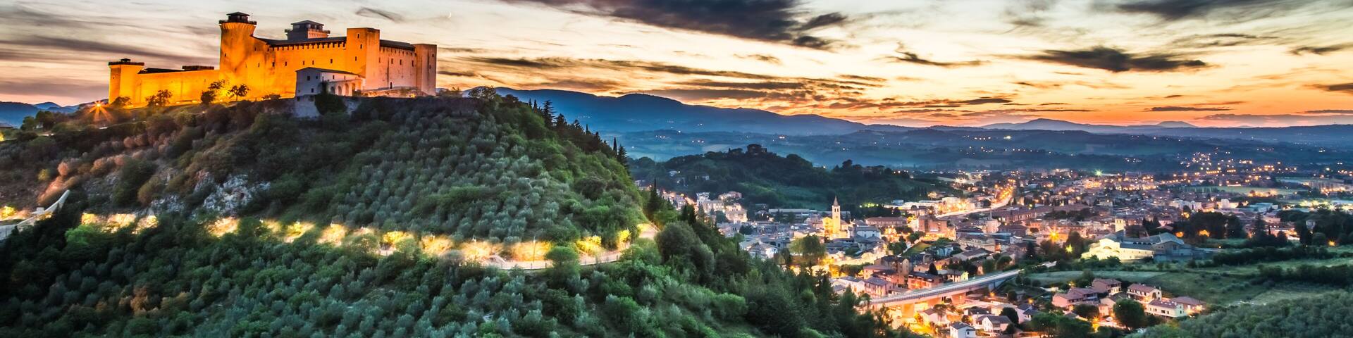 A castle on a hill overlooking a town at sunset.