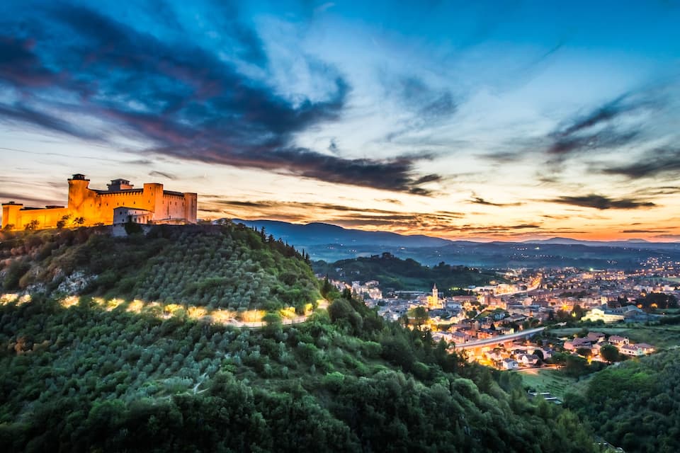 A castle on a hill overlooking a town at sunset.