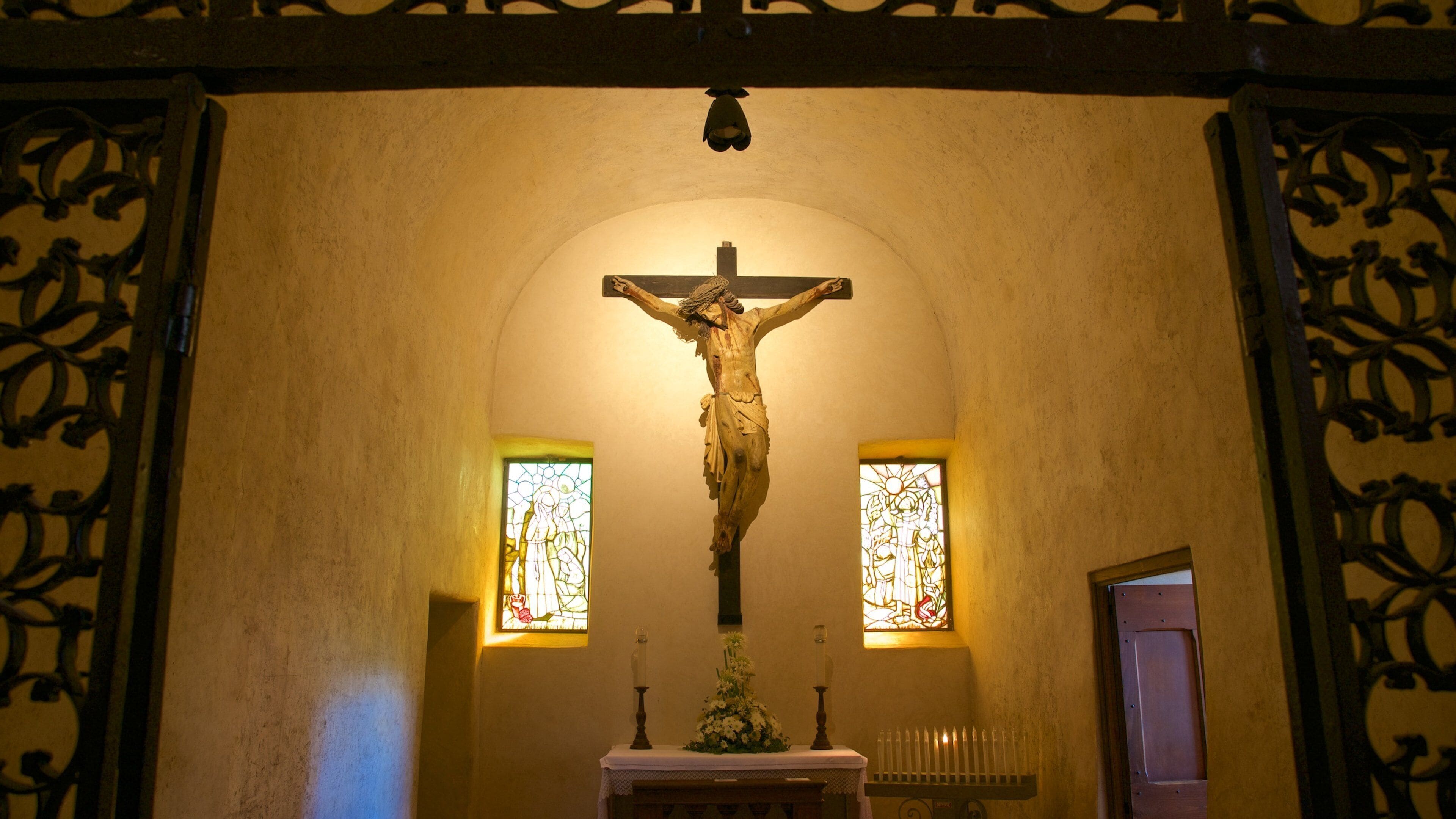 Een krucifixie in een kerk met glas-in-loodramen en versierde ijzerwerk.