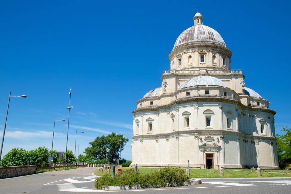 A large domed building with a central entrance, surrounded by a paved area and street lamps.