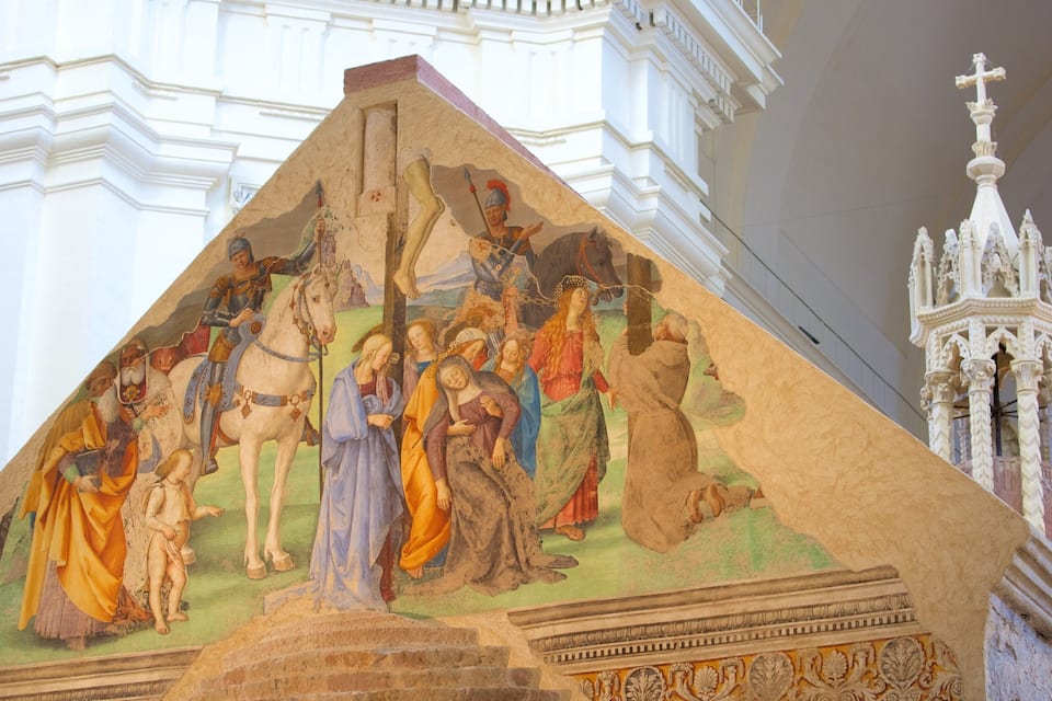 A fresco mural depicting a historical scene with figures in armor and religious figures, set against a white architectural background with a bell tower.