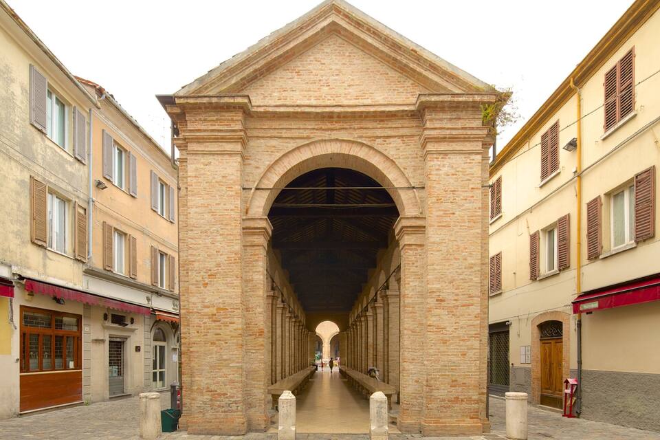 A historic stone archway with a central passageway flanked by buildings with shuttered windows.