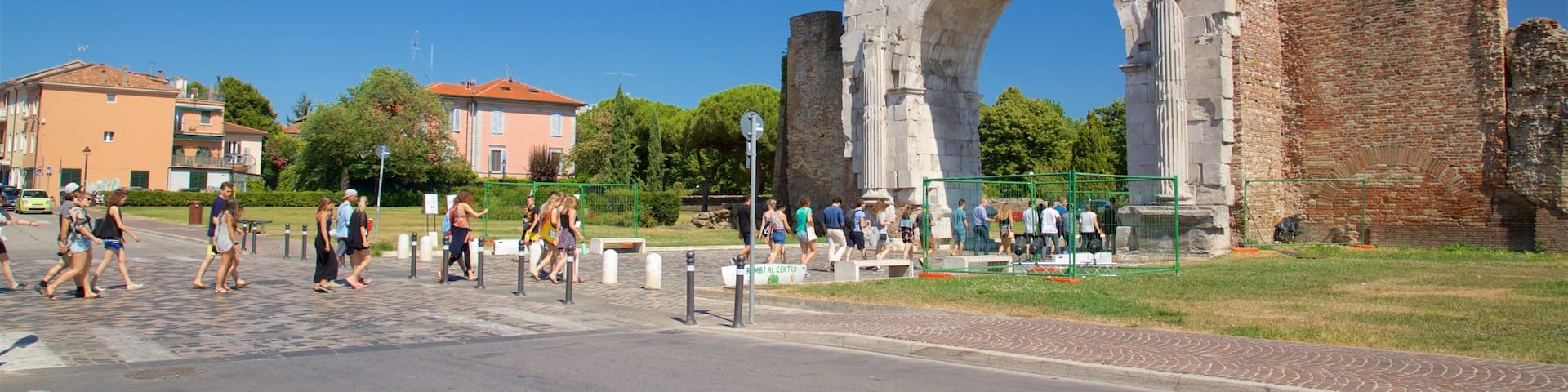 A historic stone archway with battlements, surrounded by modern buildings and a clear blue sky.