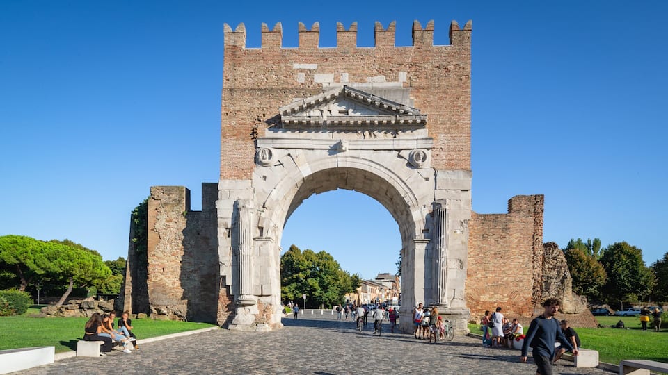 An ancient stone archway with battlements, surrounded by cobblestone streets and greenery.