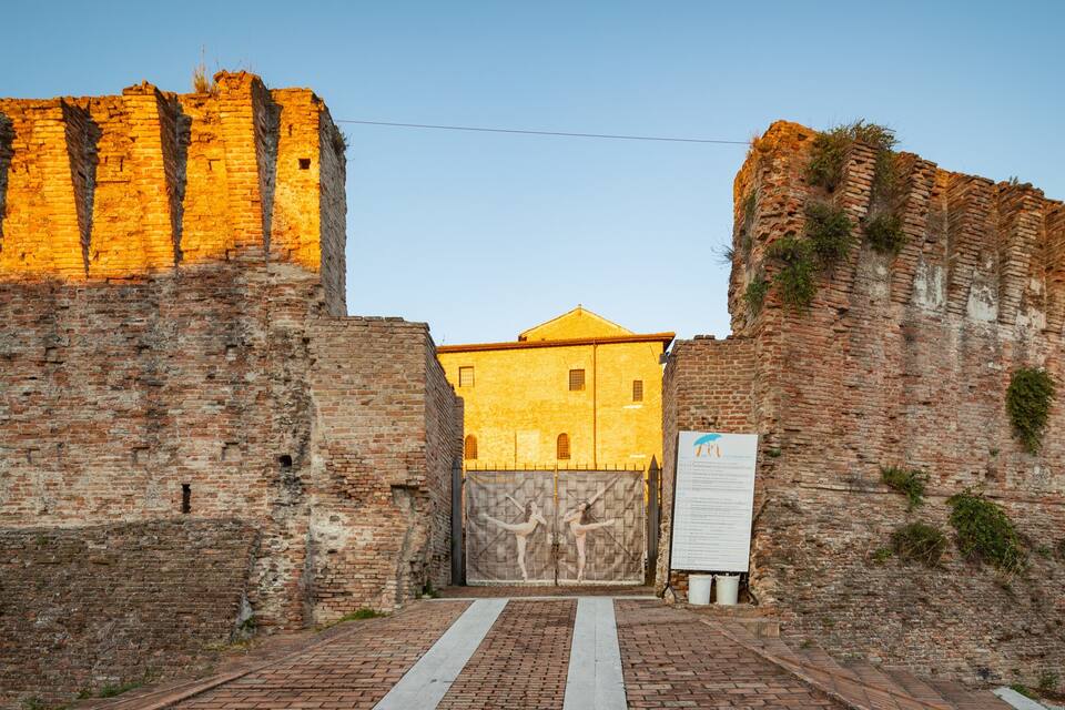 A historic stone gate with a yellow building in the background.