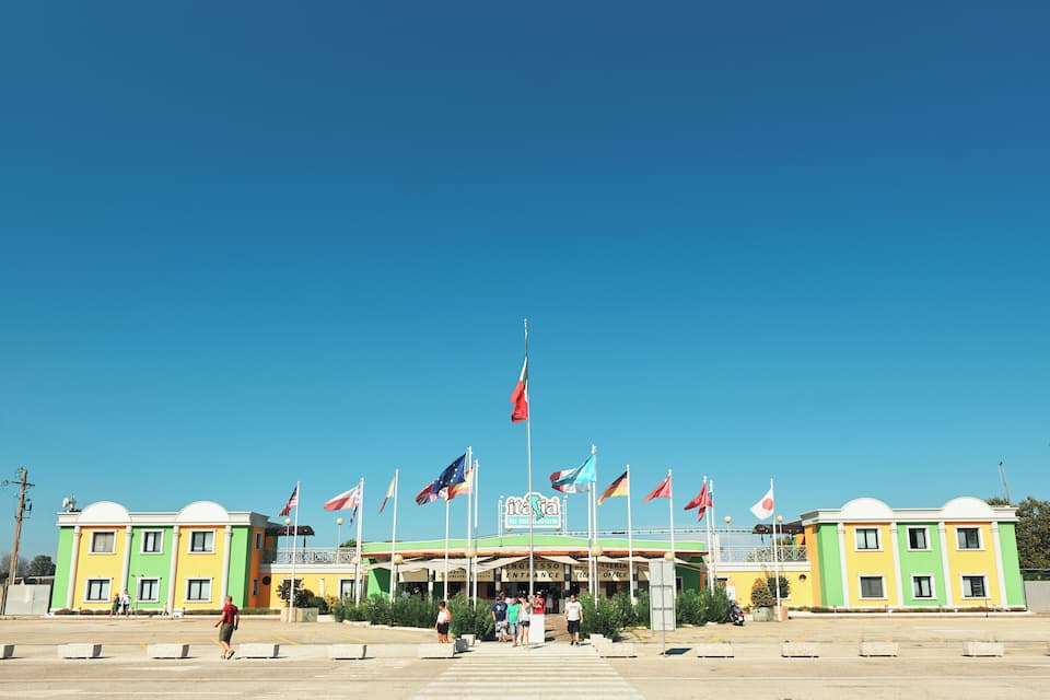 A colorful building with multiple flags, a clear blue sky, and a few people walking in front.