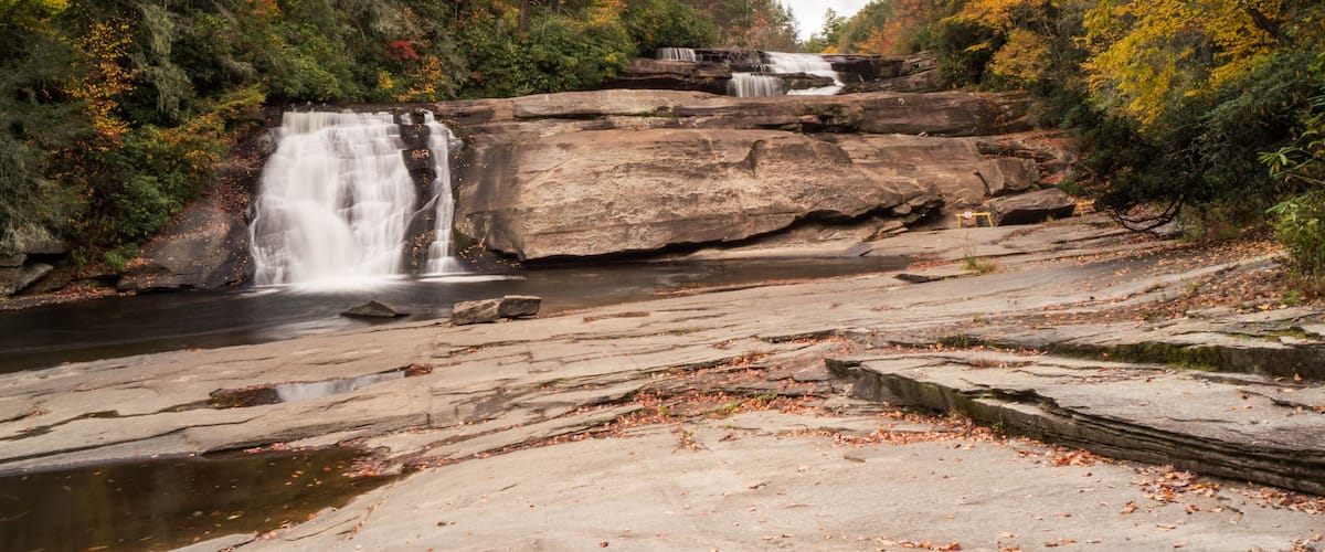 A waterfall cascading over a rocky ledge into a river, surrounded by autumn foliage.