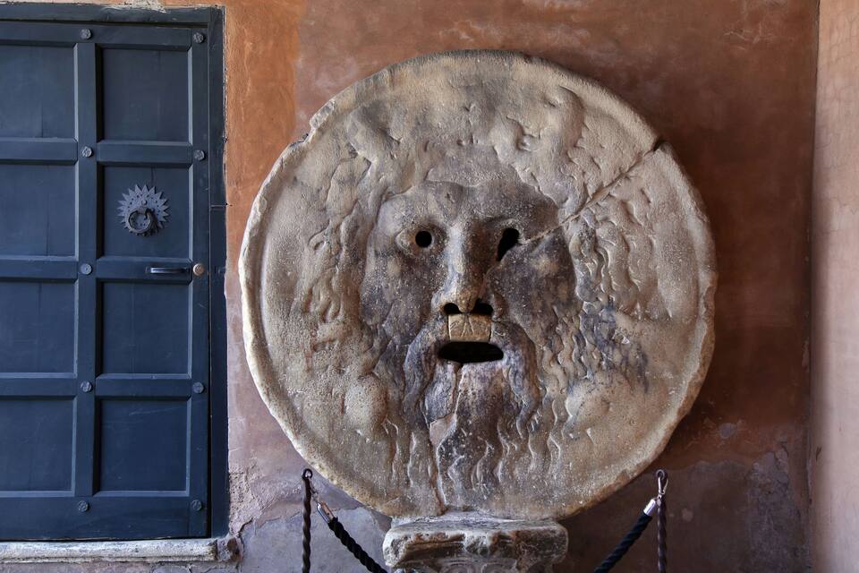 A stone head with a lion's face mounted on a wall next to a black door.