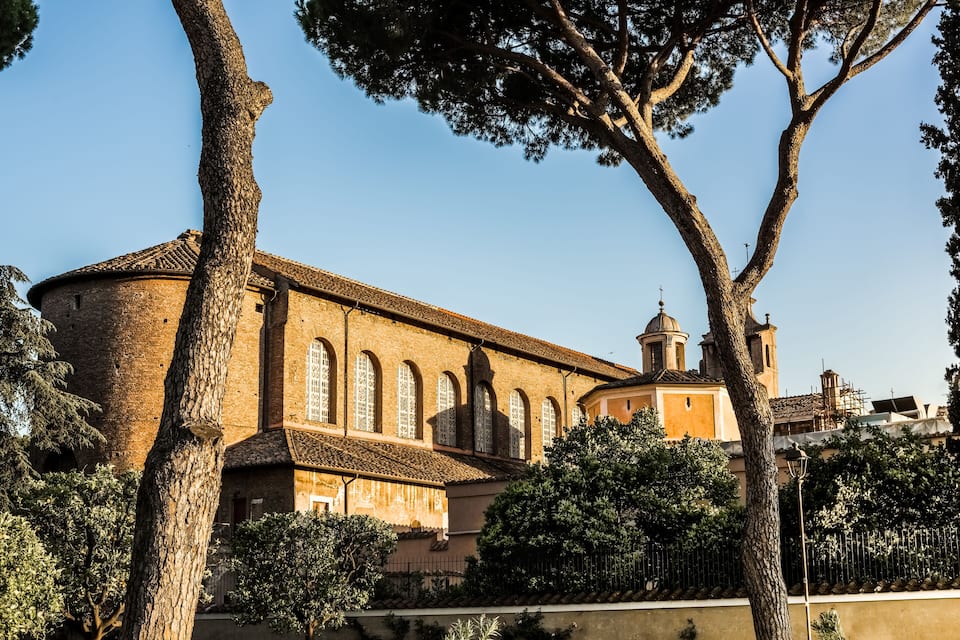 A historic building with arched windows and a bell tower, surrounded by trees and a fence.
