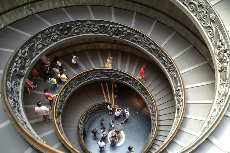 Un magnifique escalier en colimaçon, orné de rampes de métal travaillées et doté d’une plateforme circulaire centrale.