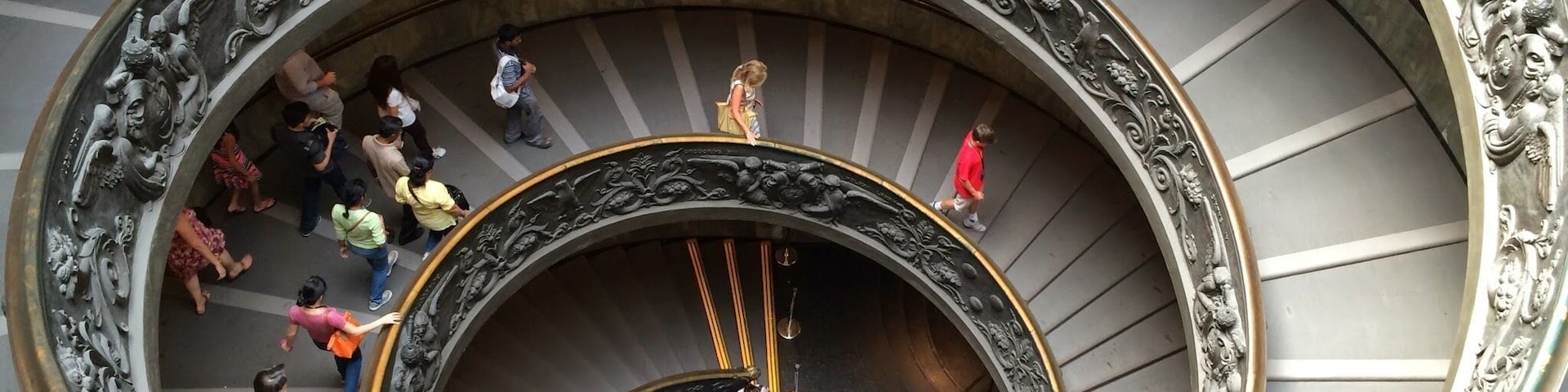 Una majestuosa escalera en espiral con barandillas de metal ornamentadas y una plataforma circular central.