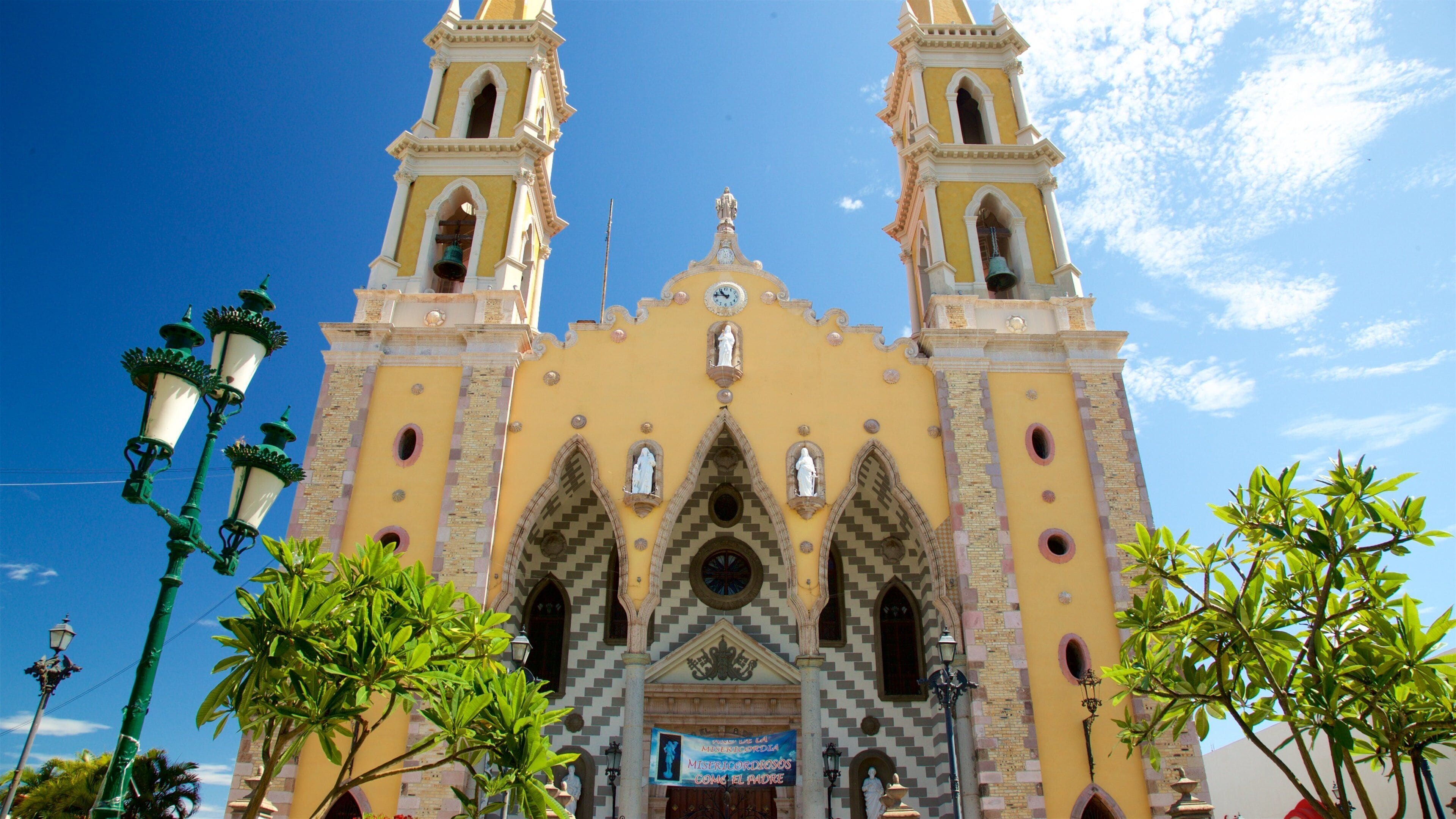Una iglesia histórica con dos torres, un reloj y un cartel frontal.