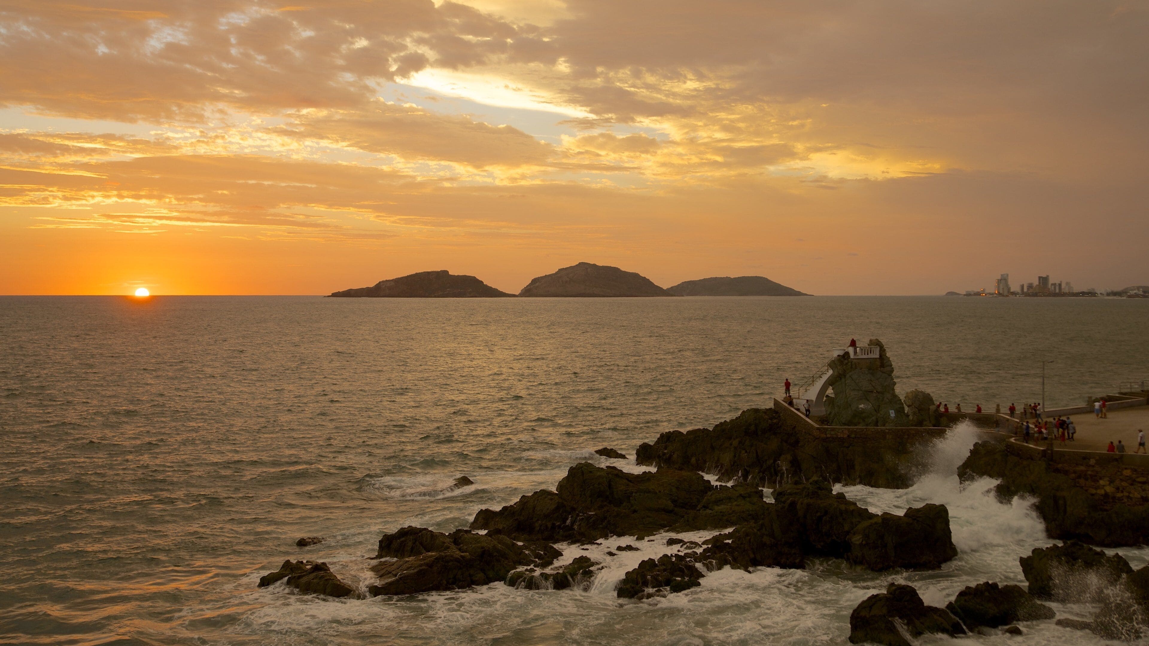 A sunset over the ocean with rocky outcrops and distant islands.