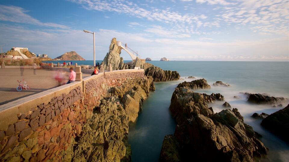 A rocky coastal walkway with a stone wall, a metal street lamp, and a distant view of the sea.