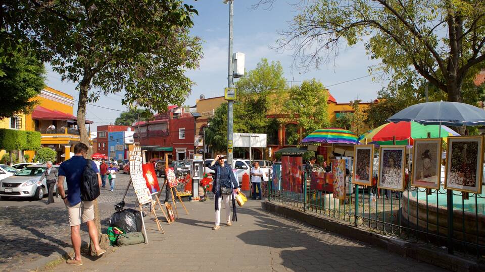 A street with art stalls, a fountain, and buildings in the background.