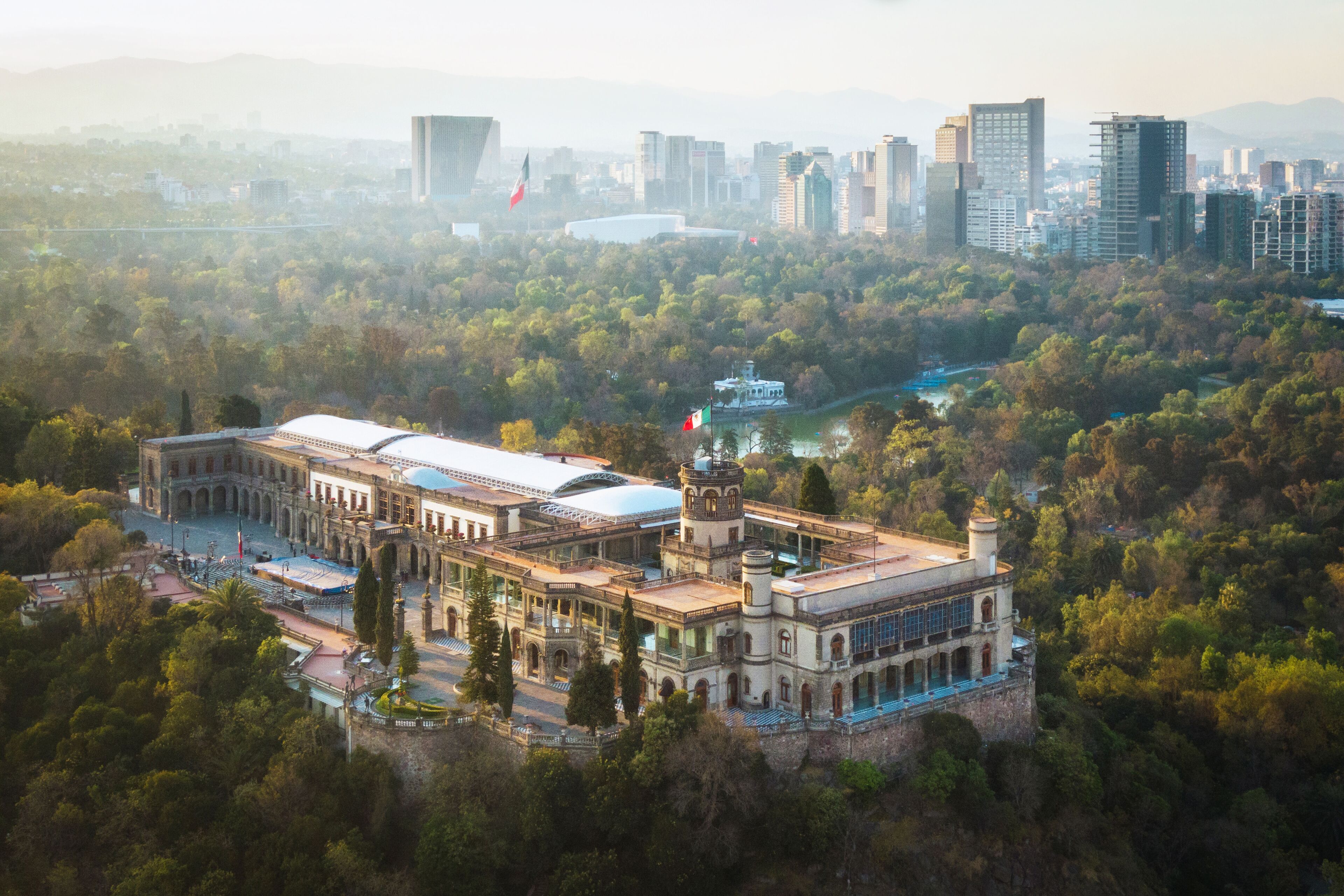 A historic building surrounded by lush greenery, with a cityscape in the background.