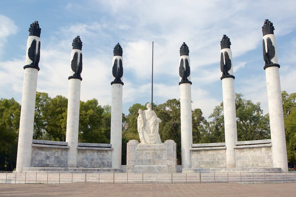 A monument with six columns, each topped with a statue of a winged figure, and a central statue of a seated figure.