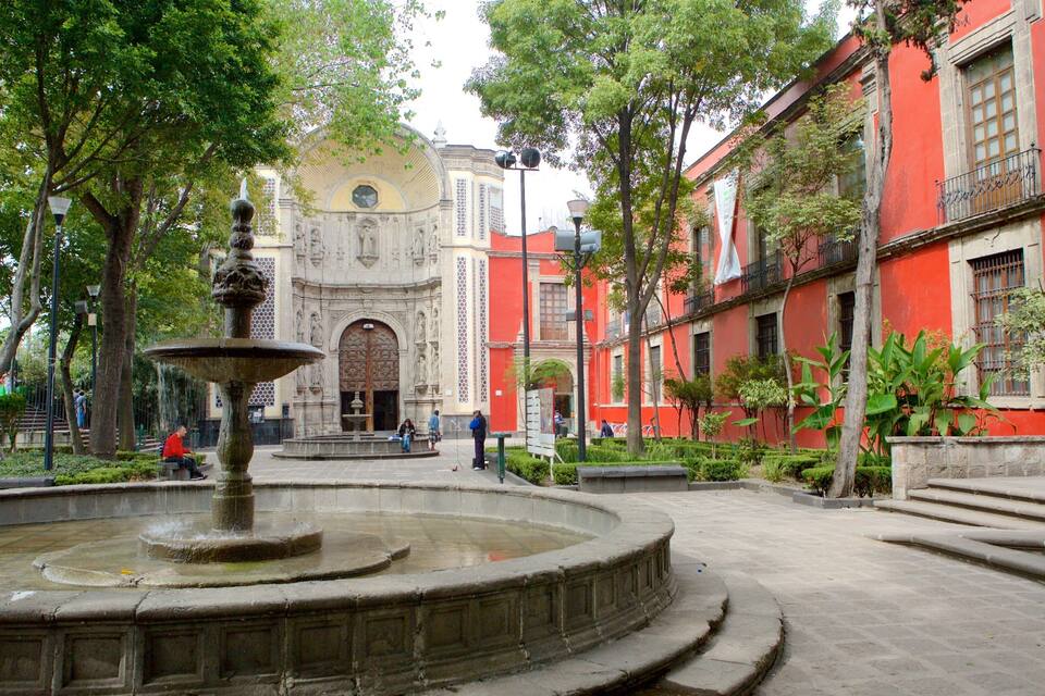 Um pátio com uma fonte, um edifício vermelho com uma cúpula amarela e pessoas passeando.