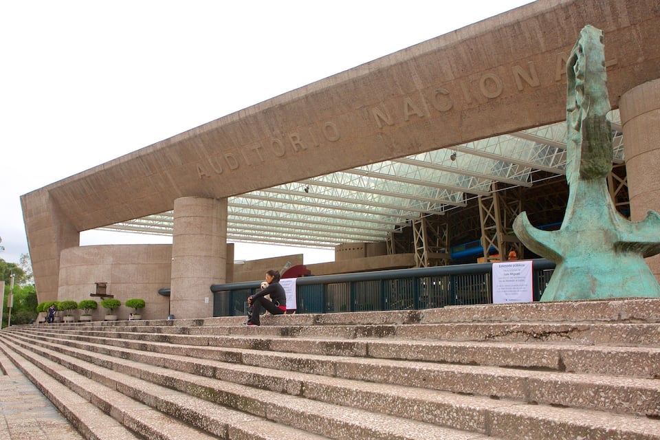 A large stone building with steps leading up to it, a large metal sculpture, and a sign with text.