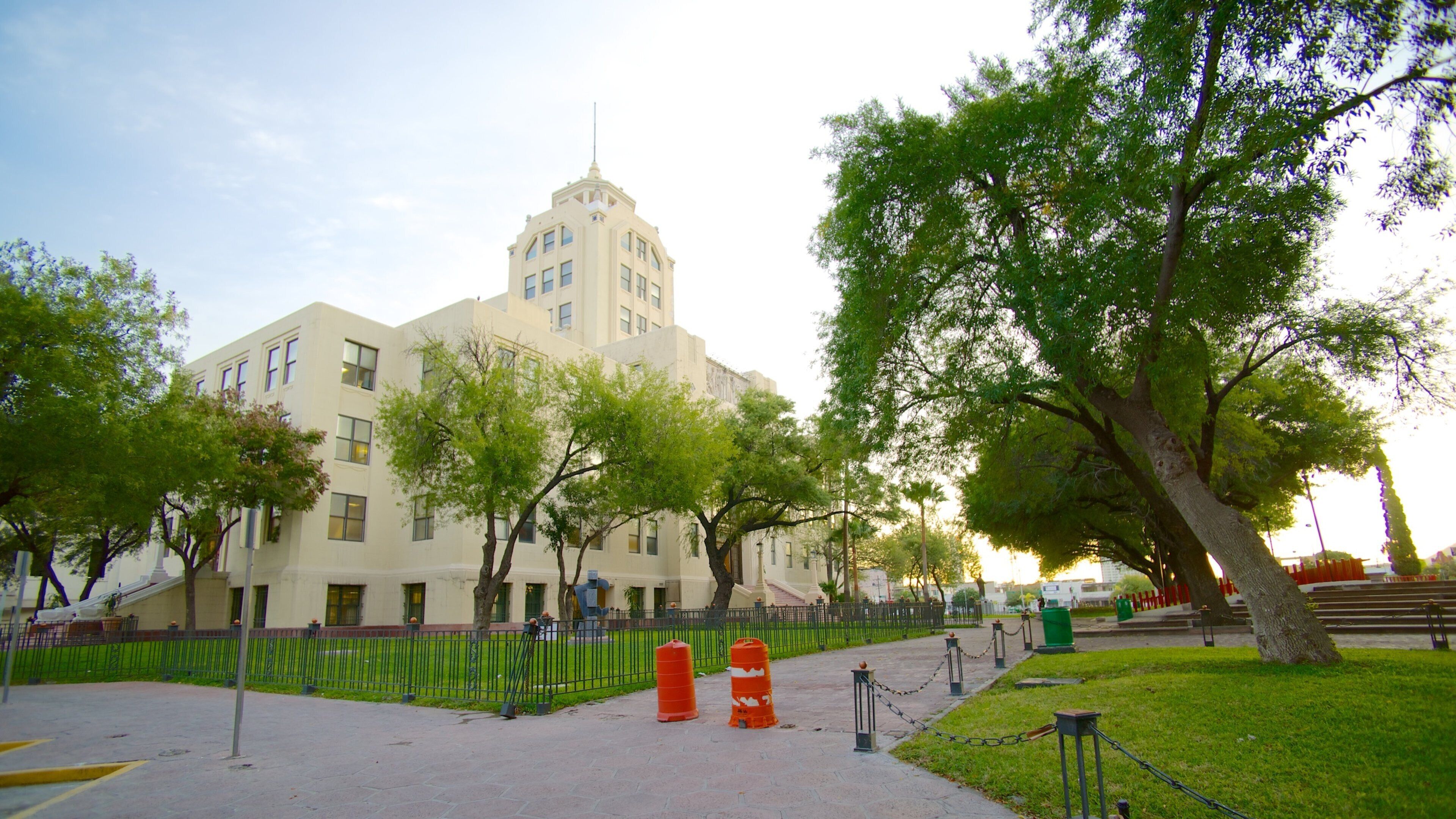 A historic building with a tower, surrounded by trees and a fenced area with orange traffic cones.