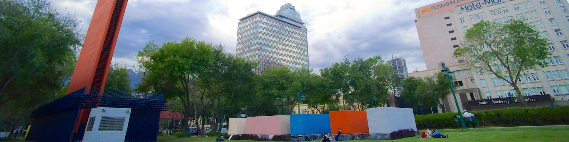A park with a tall red sculpture, trees, and a building with 'Hotel Monterrey' signage.