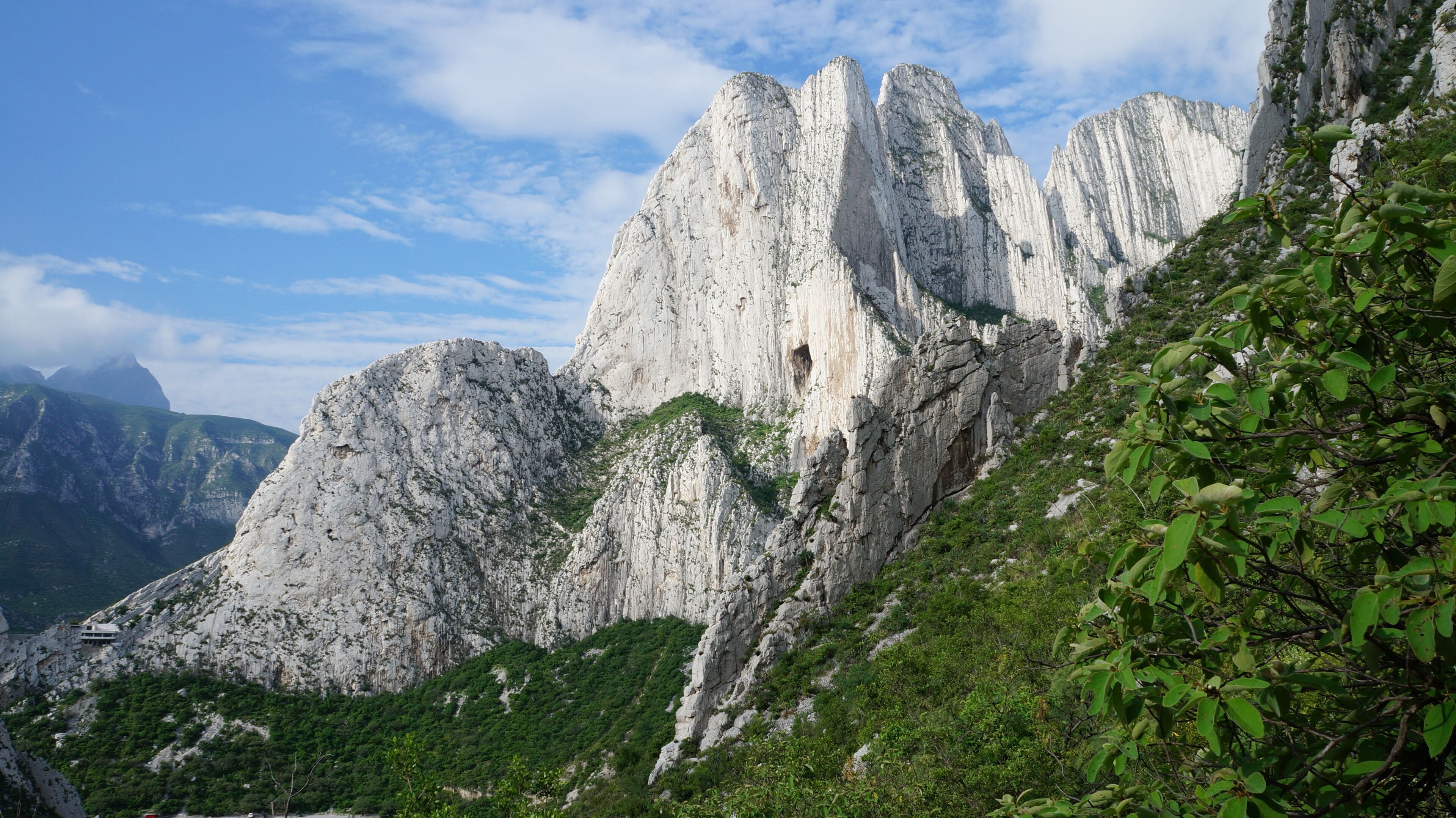 A rugged mountain landscape with prominent white rock formations and lush green vegetation.