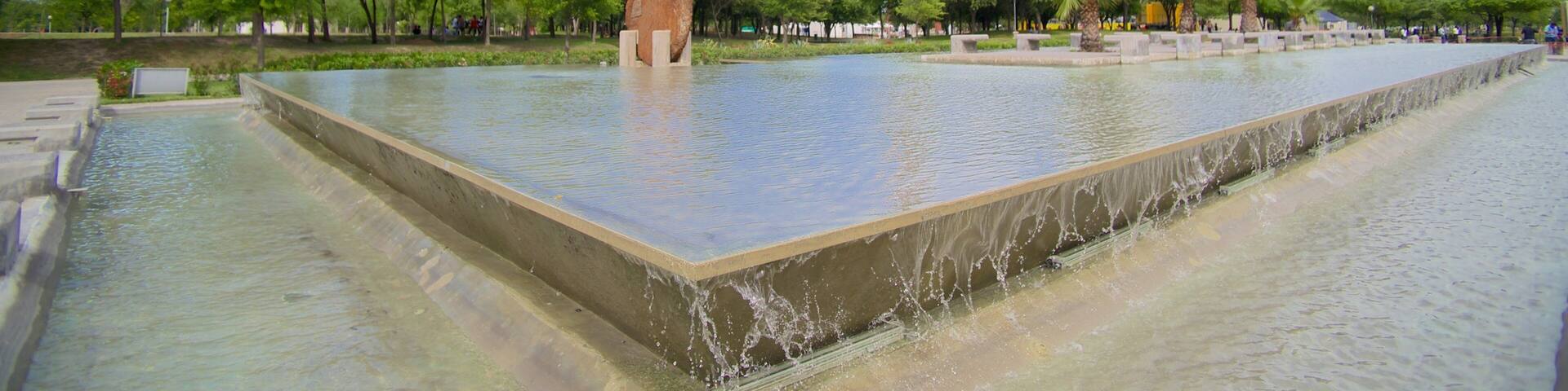 A water feature with a central island, a Ferris wheel, and a tall tower in the background.