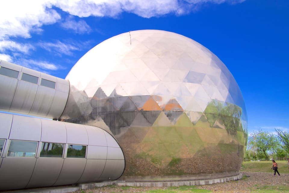 A large geodesic dome structure with a metallic exterior and a reflective surface, set against a clear blue sky.