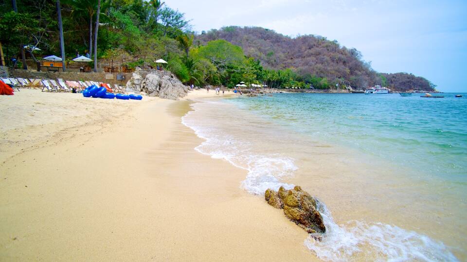 A sandy beach with clear water, lounge chairs, and a rocky outcrop.