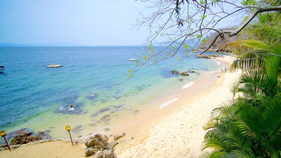 A beach with clear turquoise water, sandy shore, and rocky outcrops.