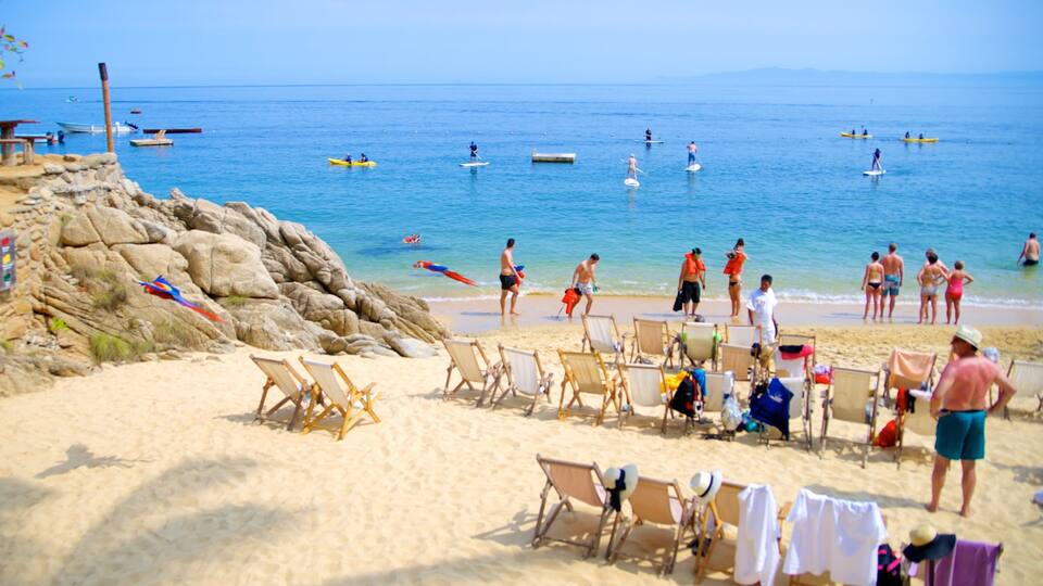 A beach with people paddleboarding, kayaks, and a rocky shoreline.