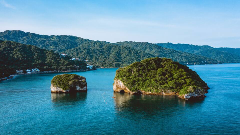 Two large islands with dense green vegetation surrounded by calm blue waters and a backdrop of forested hills.