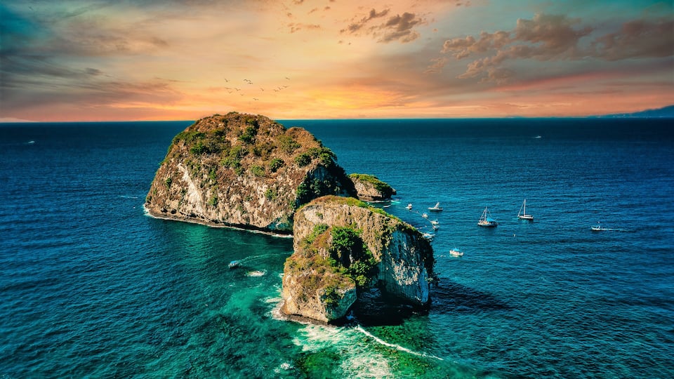 A coastal landscape with clear turquoise waters, rocky formations, and boats.