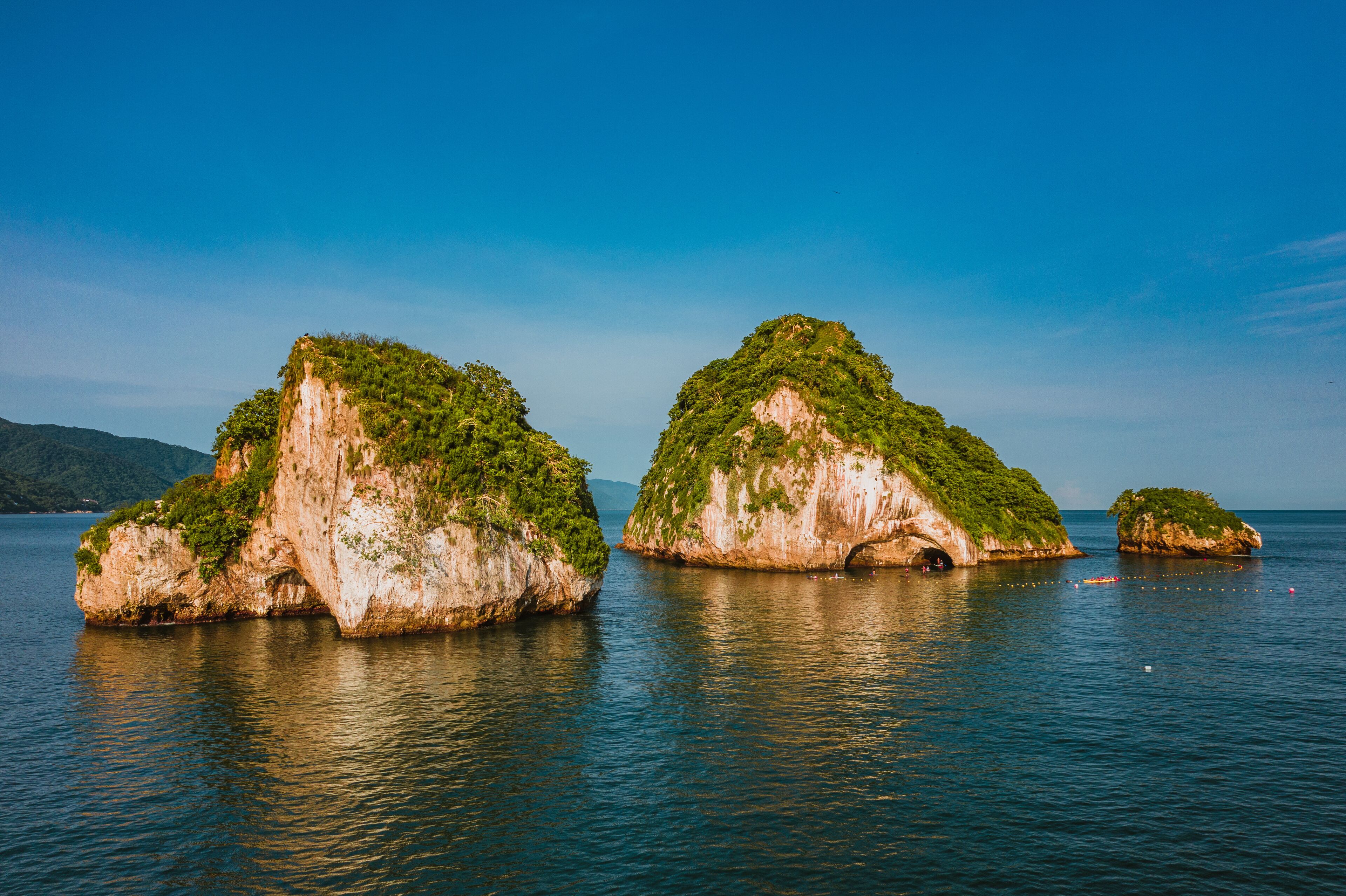 Three rock formations with greenery on top, surrounded by calm water.