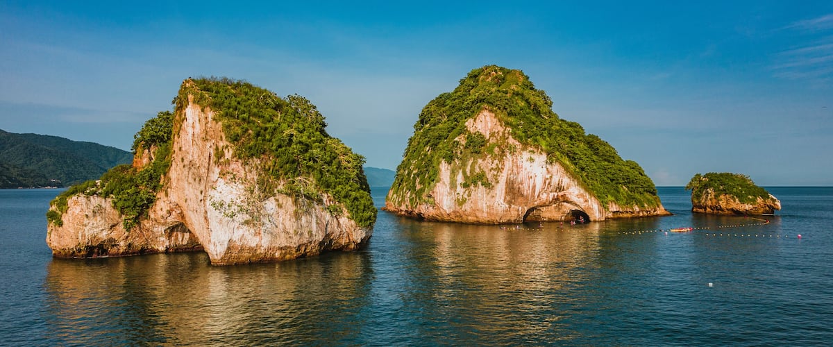 Three rock formations with greenery on top, surrounded by calm water.