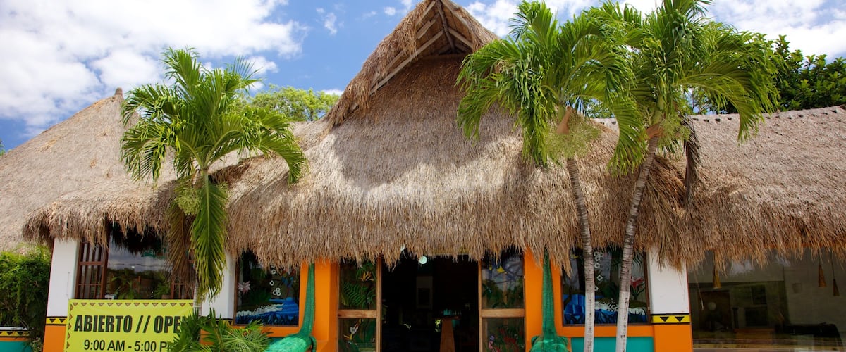 A thatched-roof building with palm trees, a signboard, and a crocodile statue.