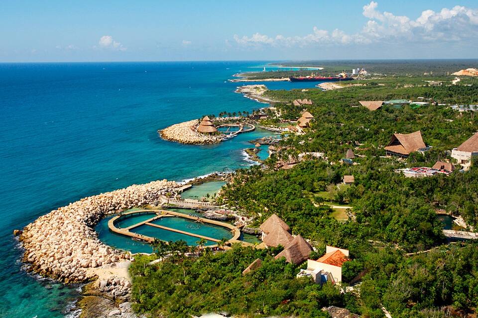 Un complejo turístico frente al mar con aguas azul cristalina, un litoral rocoso y edificios con techo de paja.
