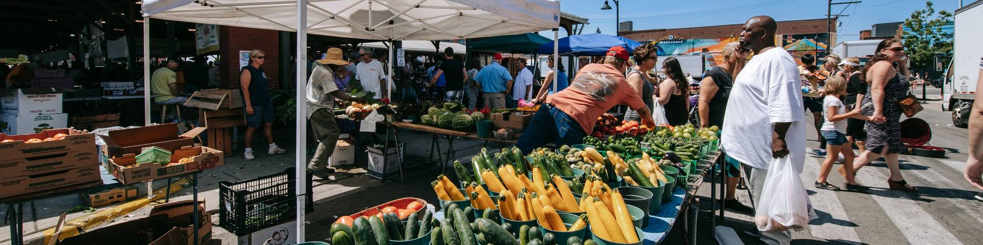 An outdoor farmers market with various vegetables and fruits on display.