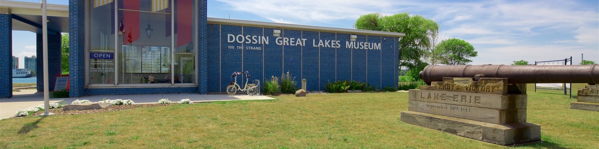 The Dossin Great Lakes Museum building with a flagpole, a cannon, and a sign indicating the museum's name and address.