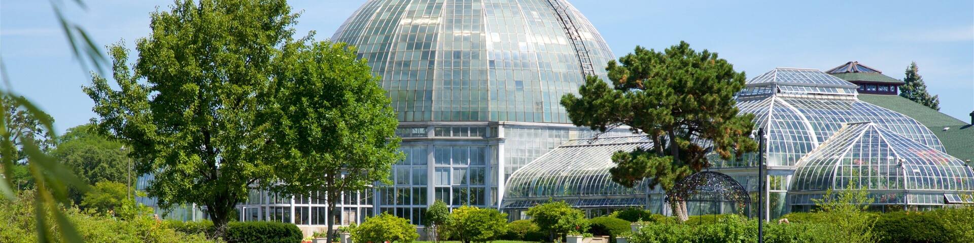A large glass greenhouse with a dome roof, surrounded by lush greenery and a calm pond.