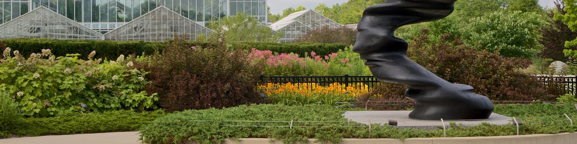 Una escultura en un jardín con un invernadero al fondo.