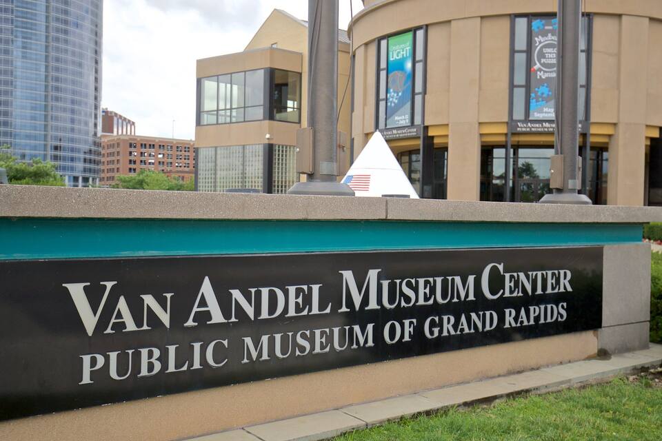 The Van Andel Museum Center sign with a view of modern buildings in the background.