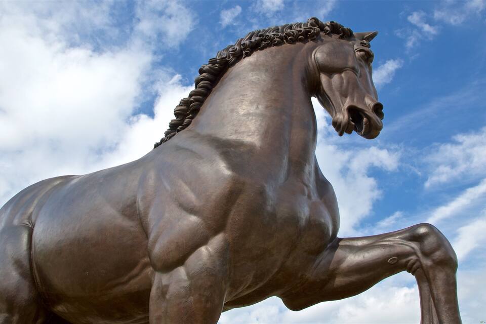 A bronze horse statue with a mane, set against a partly cloudy sky.